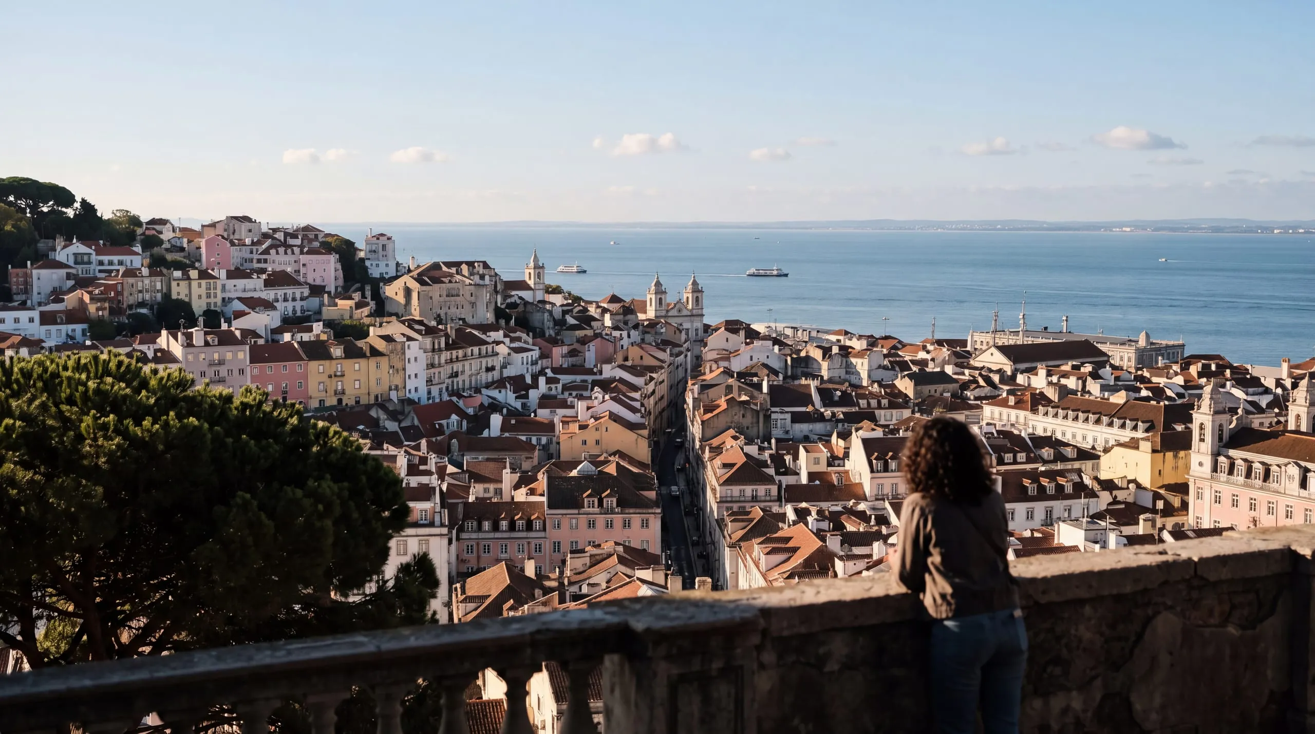 A European city seen from a terrace in the hills in the morning, rooftops, a river and the sea to the horizon.